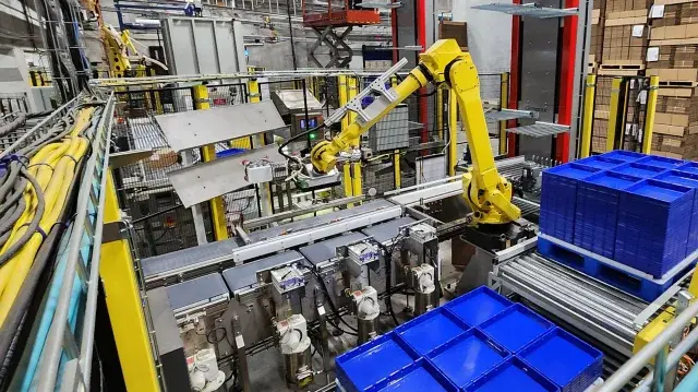 automatisiertes Verpackungssystem - gelber Roboterarm - blaue Paletten