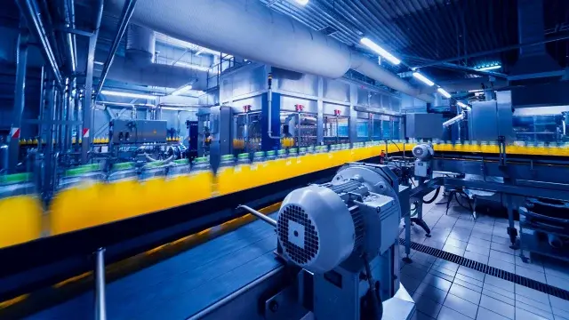Interior beverage factory showing bottles of yellow juice on conveyor belt.